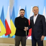 Володимир Зеленський і Дональд Туск тиснуть руки на тлі прапорів України та Польщі