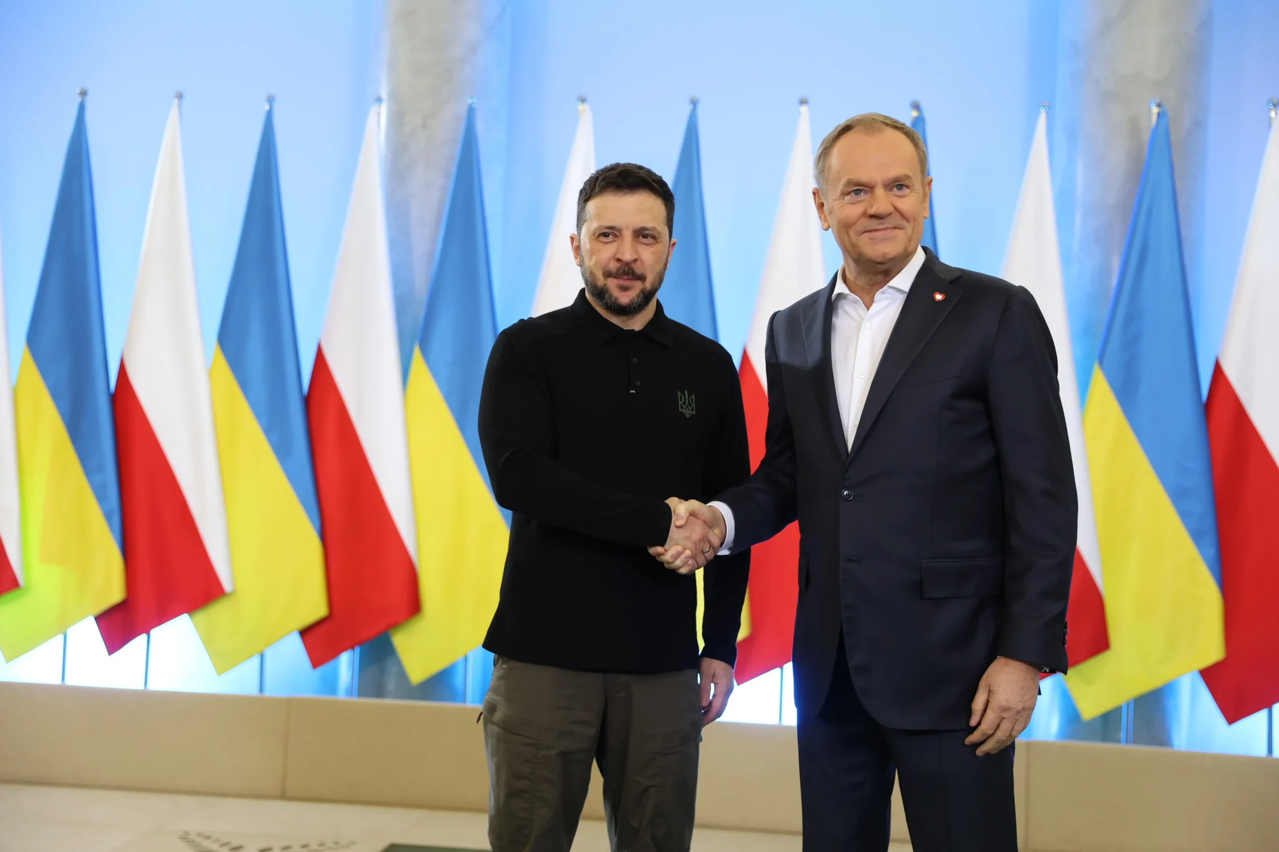 Володимир Зеленський і Дональд Туск тиснуть руки на тлі прапорів України та Польщі