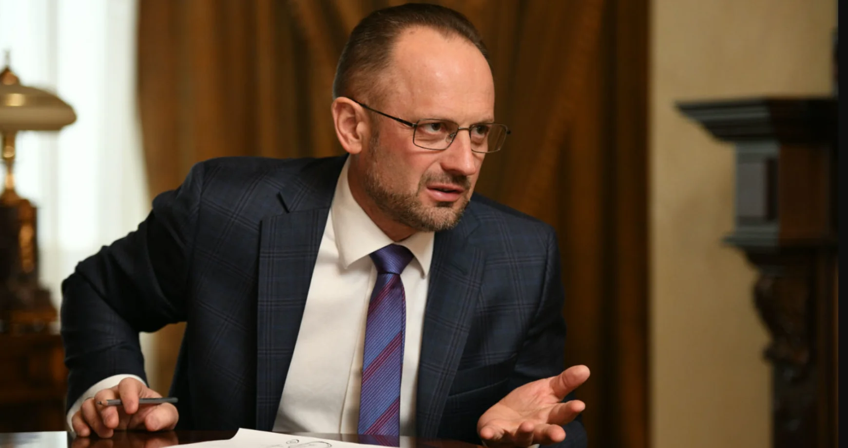 Роман Безсмертний у синьому костюмі жестикулює за столом під час розмови
