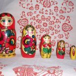 Пять традиційних російських матрьошок різного розміру на білій скатертині з червоним орнаментом