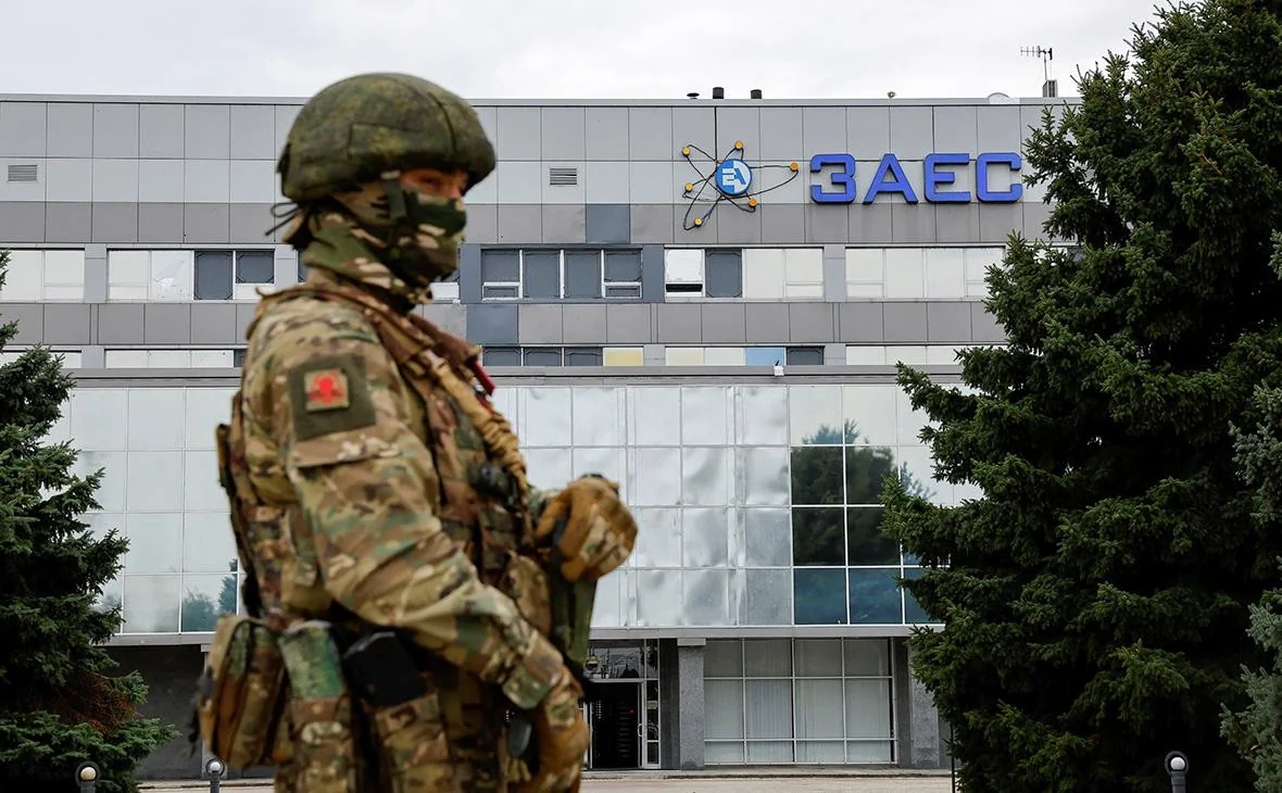 Російський солдат у камуфляжі стоїть перед будівлею Запорізької АЕС