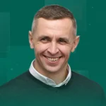 Усміхнений чоловік з коротким волоссям у зеленому светрі поверх білої сорочки на зеленому тлі
